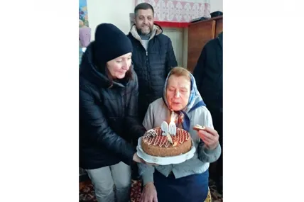Вчителька-ювілярка задуває свічки на святковому торті від своїх колишніх учнів.