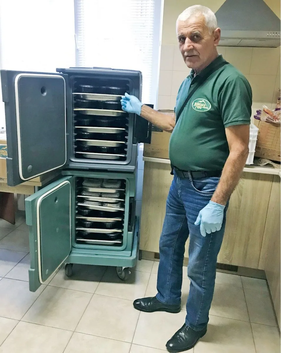 Пан Михайло тягне величезну духову шафу, в якій на полицях порційно розміщені перша і друга страви.
