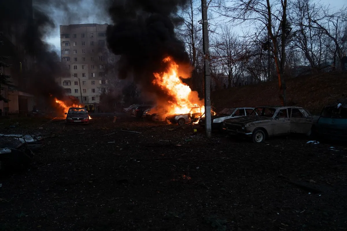 Палаючі автомобілі, які горять внаслідок вибухів при ранковому ракетному обстрілі Львова. Навколо уламки пошкодженого будинку