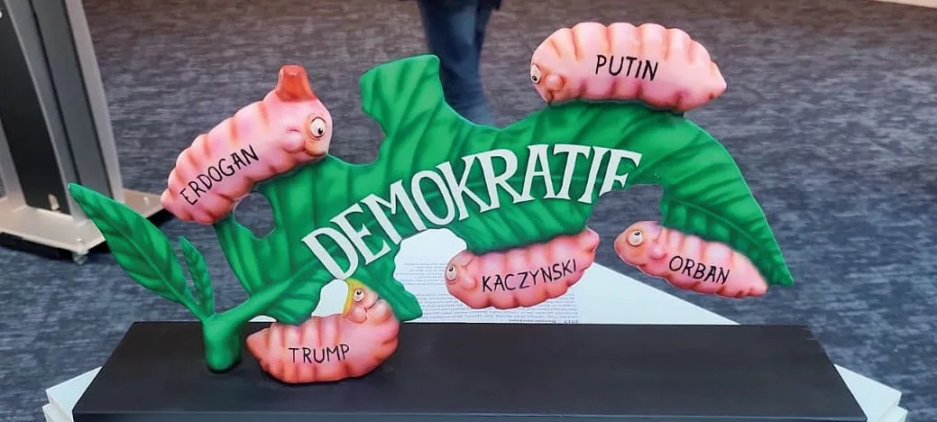 Зелений листок із написом «Демократія» пожирають Качинський, Орбан, Трамп, путін і Ердоган, зображені як голодні личинки